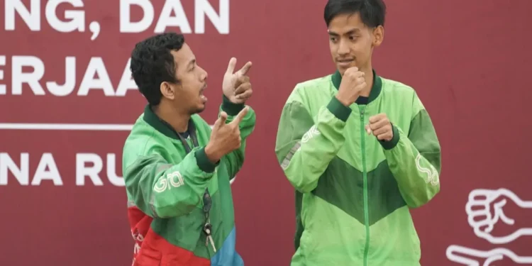 Pengemudi ojol Tuli beristirahat di pinggir jalan dengan jaket ojek online dan helm di Jakarta Timur